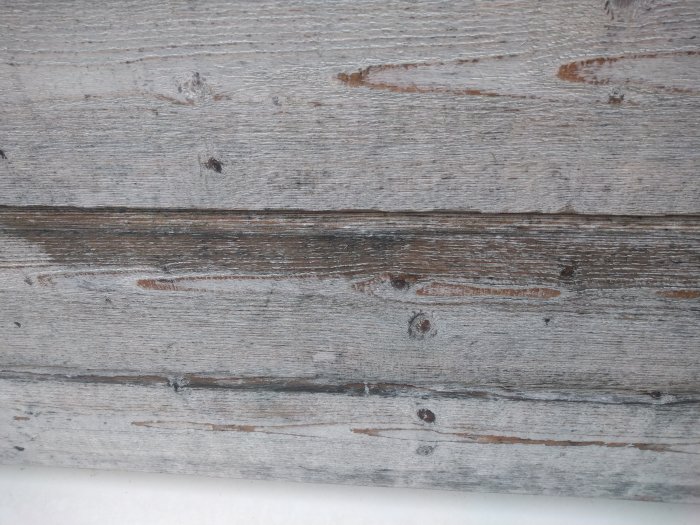 Närbild av en trävägg med ojämnt applicerad grå färg som ser sliten och fläckig ut.