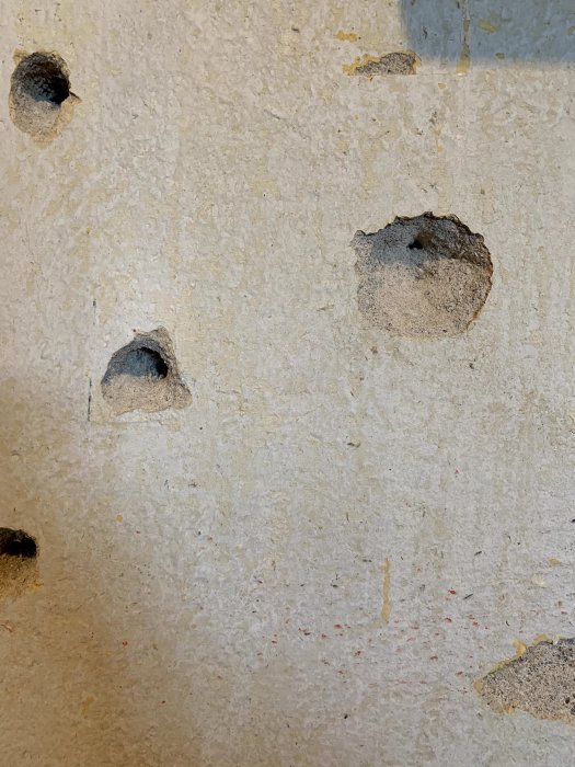 Vägg med små skadade områden och kratrar för tapetförberedelse.