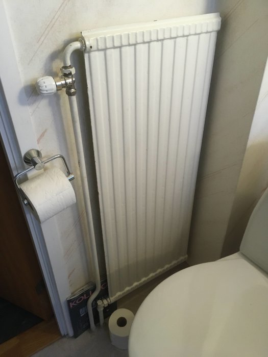 Ett vitmålat radiator-element bredvid en toalett i ett litet badrum, med förfrågan om att ersätta det med golvvärme.
