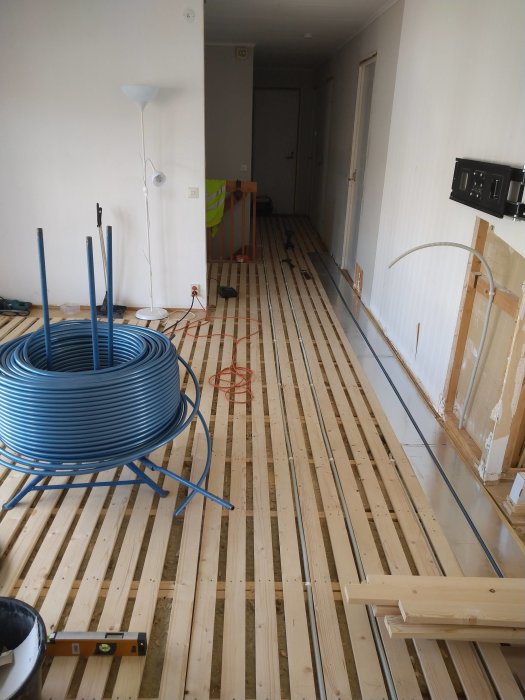 Installation av golvvärme med blå PEX-rör på träreglar och tomrör för uttag i renoverat rum.