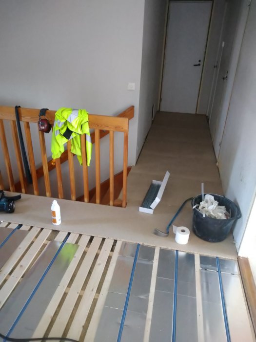 Installationsfas för golvvärme med synliga rör och reglar på ett övervåningsgolv, tomrör och arbetsmaterial.