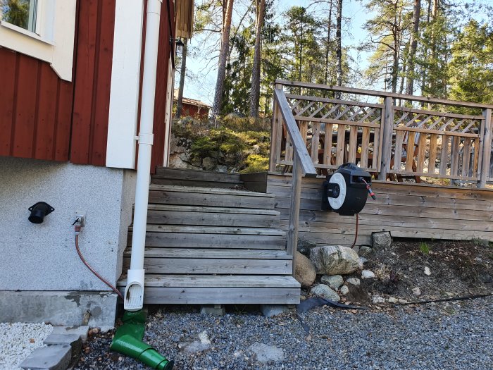 Nybyggd trätrappa och altan vid röd stuga med omgivande skog.