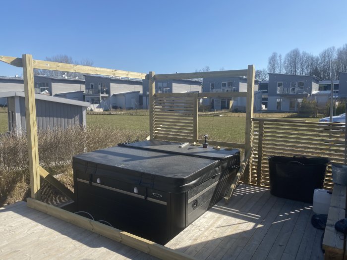 Inbyggnad av ett spabad på en träterrass med staketpaneler och pågående konstruktion, i ett bostadsområde en solig dag.