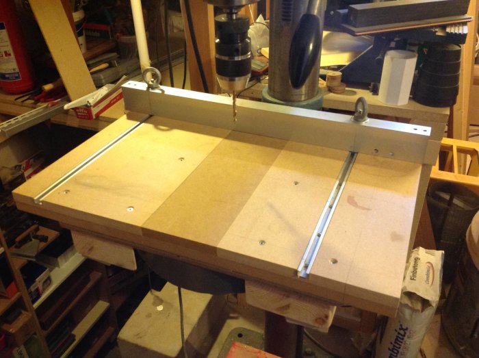 Verkstadsbord med pelarborr ovanför och en anordning för att borra i aluminiumskena på bordet.