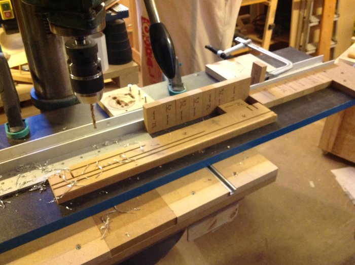 Verkstadsarbetsbänk med ett borrprojekt, inklusive hålmall, skruvdragare och märkta träbitar.