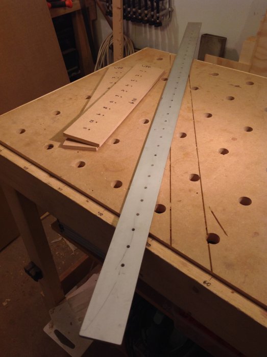 Nyborrad hålmall i aluminium och en MDF-mall på ett arbetsbord i en verkstad.