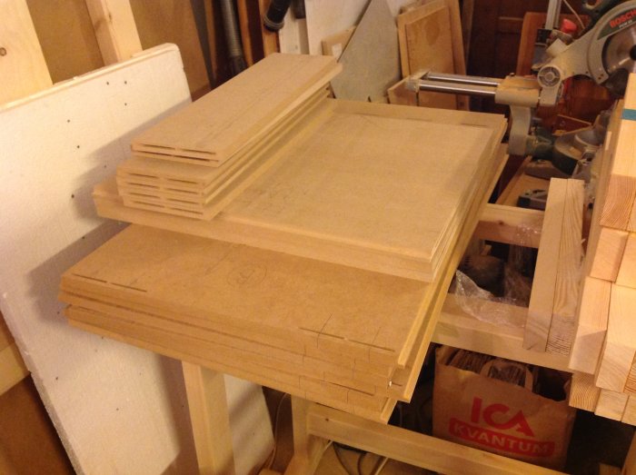 Trave med MDF-skivor för beredning av hålmallar i en verkstadsinställning, märkta och staplade för bearbetning.