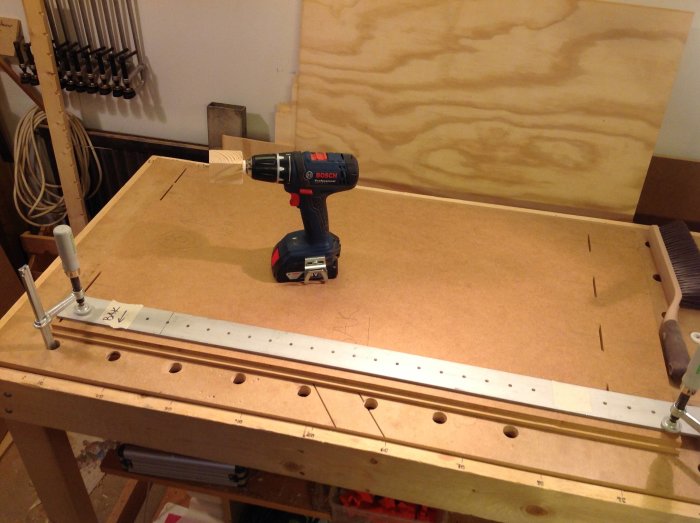 Verkstadsbord med ny hålmall, skruvdragare och mätklossar för borrning.