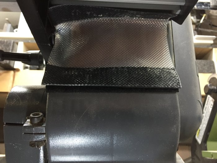 En slipmaskin med anpassat svart slipdammsskydd fäst med kardborrband.