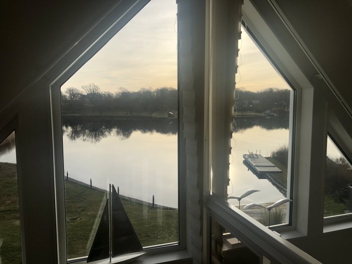 Utsikt från ett fönster över en stilla sjö och ett litet bryggan en tidig morgon.