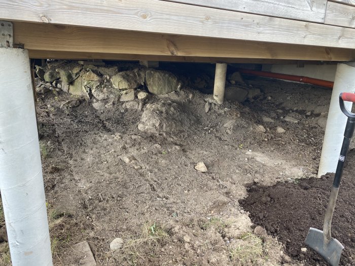 Jordyta förberedd för plantering intill trätrall med synliga plintar och stödstenmur under trallkanten.