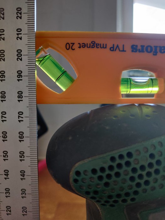 Nivåbubbla på vattenpass visar cirka 176,4 mm på måttband mot en borr.