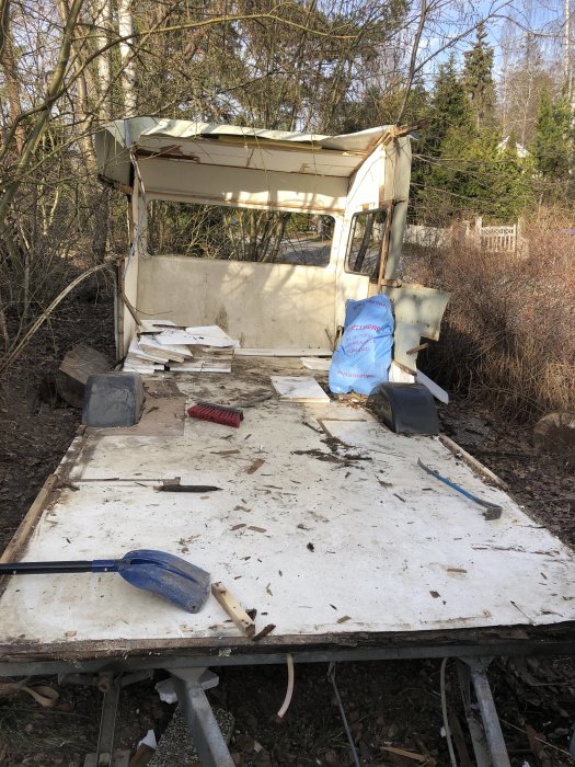 Rensat chassi från en vagn med hjul, verktyg och nedrivningsavfall på en skogsmark.