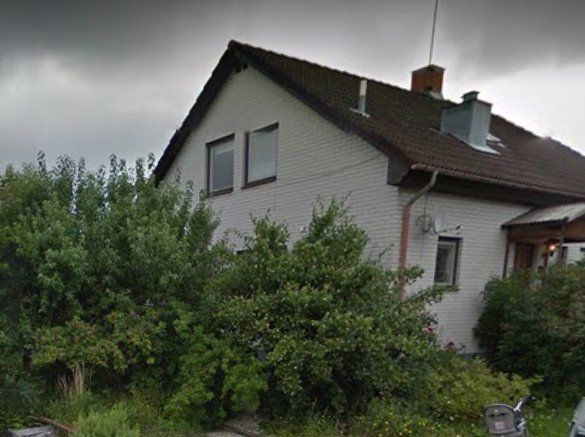 Baksida av ett vitt 1.5-planshus med uterum, omgivet av tät vegetation.