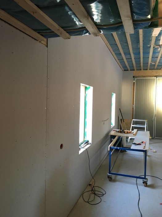 Inre vägg i garage med gipsskivor, redo för spackling, med en stege och verktyg framför.
