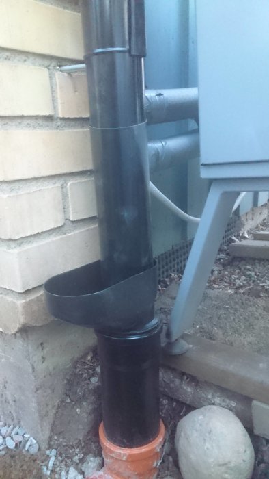 Ett nymålat svart markrör med muff och renstratt vid ett husfundament.