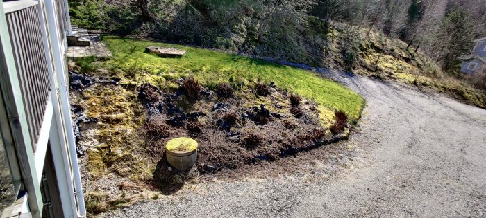 Solbelyst slänt med gräs och vildvuxna buskar intill en altan, potentiell plats för trappa och terrassering.