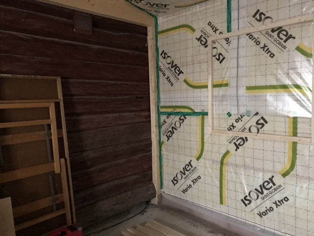 Inomhusbyggnadsutrymme med en timmervägg och väggar isolerade med ISOVER, byggnadsmaterial på golvet.
