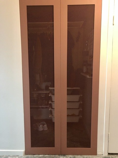 Två hemmagjorda garderobsdörrar i MDF med sträckmetallgaller, målade i brun färg och installerade med synlig klädkammare bakom.