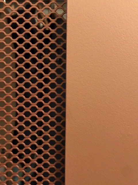 Del av en handgjord dörr med honeycomb-sträckplåtsgaller och orange täckfärg, resultat av ett DIY-projekt.
