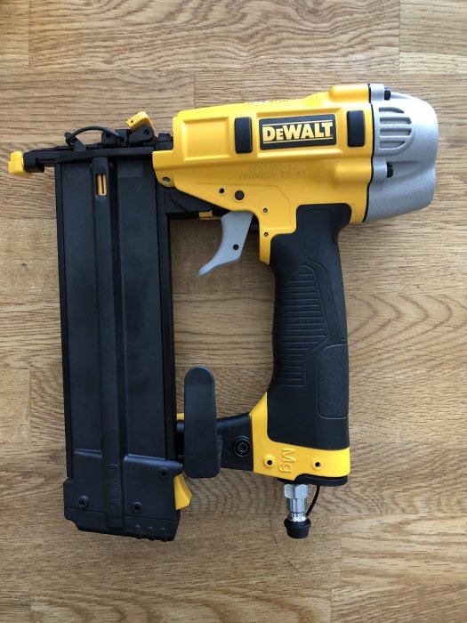 Gul och svart DEWALT DPN1850-XJ dyckertpistol för tryckluft på trägolv.