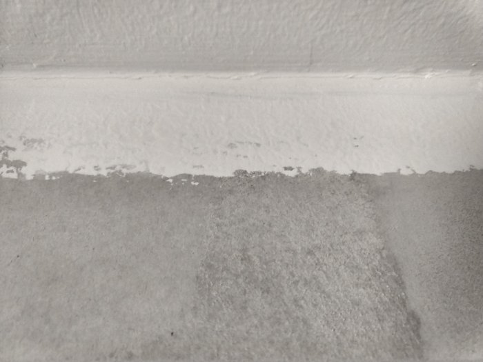 En hörn där en gipsvägg möter ett nymålat tak med synliga sprickor i fogen och avflagande färg.