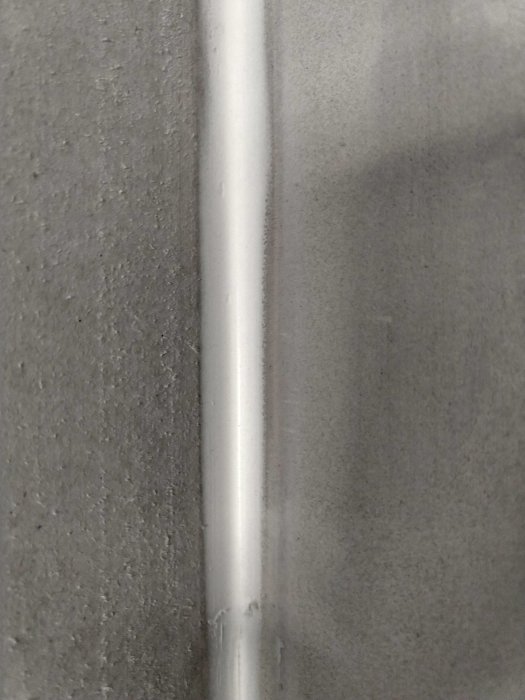 Sprickor där en vit fog möter gråmålat tak i en hörnvinkel, med osmålade väggar intill.