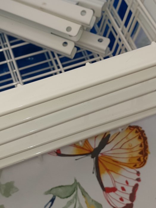 Vit Elfa korg och dess skenor i närbild med en tapet med fjärilsmönster i bakgrunden.