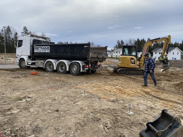 Lastbil från Rethab och grävmaskin CAT på ett byggarbetsområde med uppmärkta markeringar för anläggning.