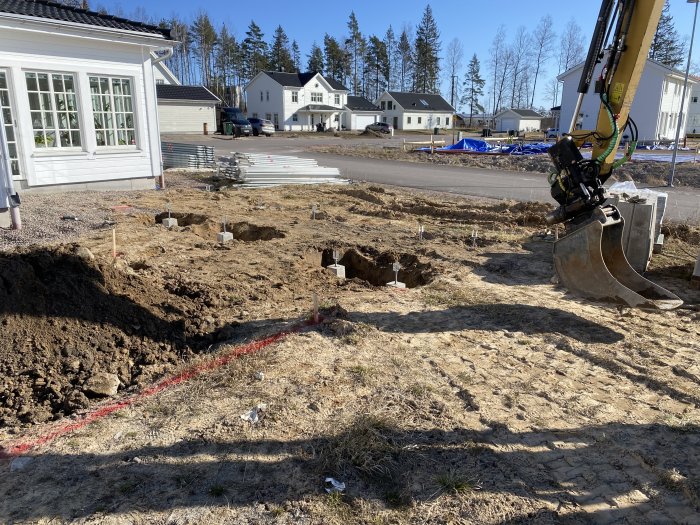 Grävmaskin vid grävt område med plintar i marken för trädäck och förberedelse för poolbygge.