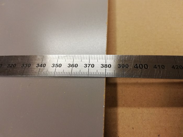 Måttband ligger på ett bord med märkning vid 390mm men mäter endast till 380mm på materialet under.