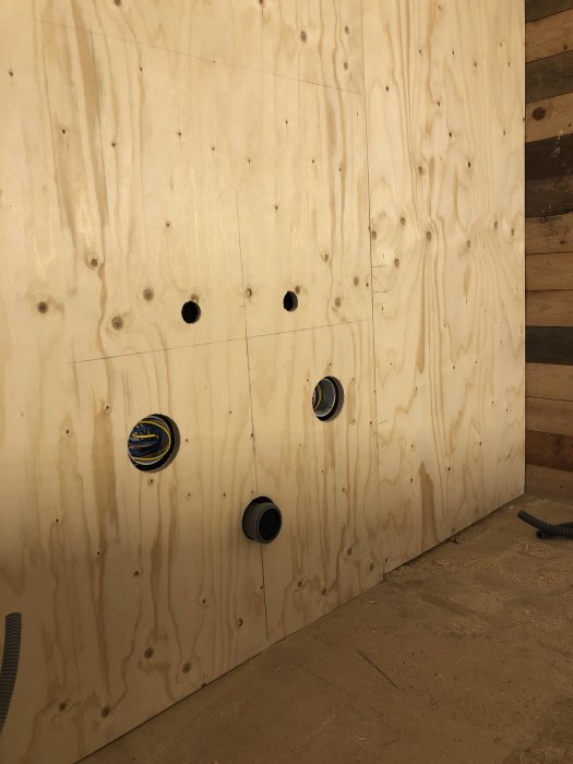 Nyinstallerad plywoodvägg med uttag och öppningar för installationer, ännu ej färdigställd.