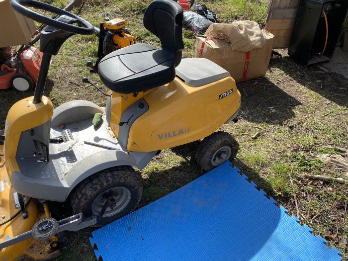 Gul Stiga Villa 12 åkgräsklippare parkerad utomhus med gräs och trädgårdsföremål i bakgrunden.