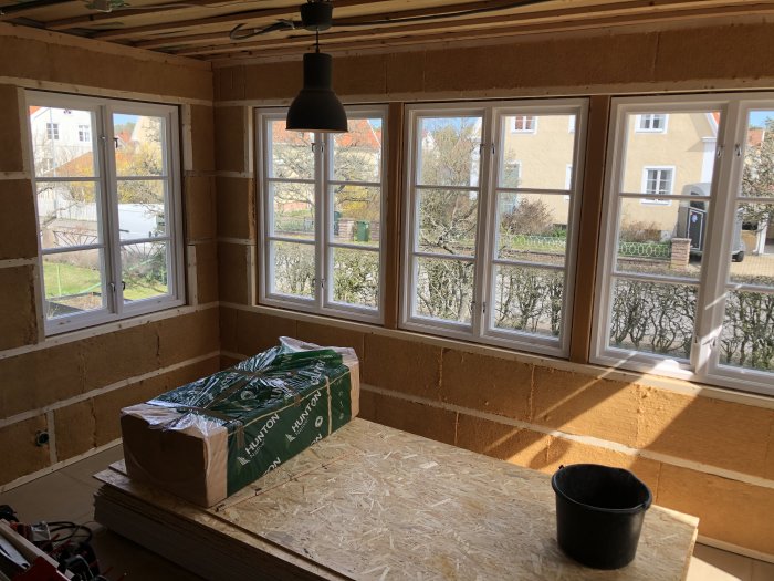 Veranda under renovering med isolerad vägg av träull och halvt färdigställt fönsterparti. Paket med träull och verktyg syns.