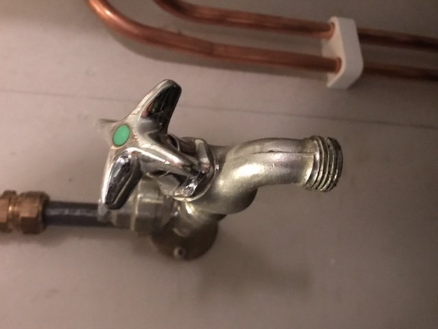Slanganslutning med en metallkran och slangklämma i ett garage, eventuell läckageproblem nära kopparledningar.