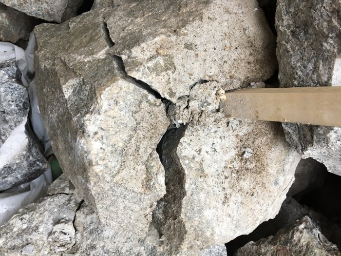 Sprängda stenblock med synliga sprickor och en mejsel insatt i en av sprickorna.