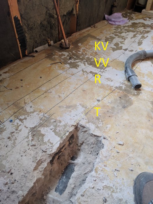 Renoveringsprojekt med uppbilat betonggolv och märkta vatten- och avloppsrör i ett hus under ombyggnad.