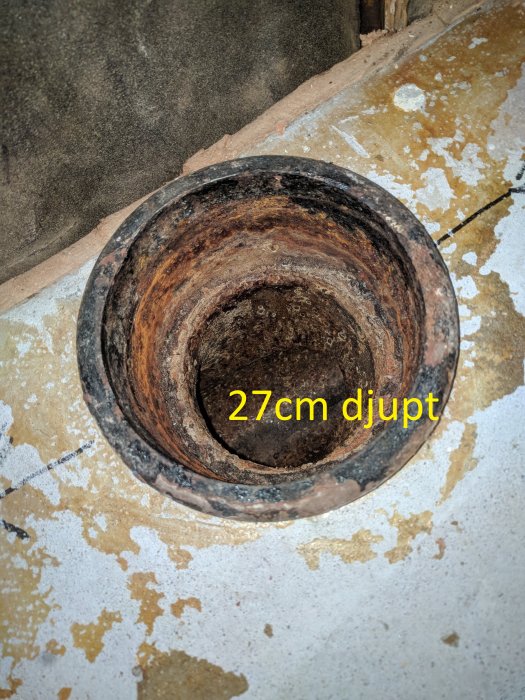 Rostig avloppsröröppning i betonggolv märkt med text "27cm djupt" som visar rörets djup till källaren.