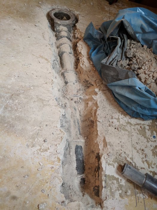 Betonggolv med uppbrutna delar och avtäckta avloppsrör vid ett pågående renoveringsprojekt.