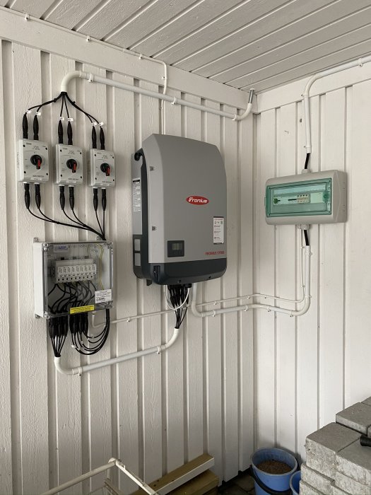 Installation av Fronius solinverter, elcentral och elmätare på vit vägg med kabeldragning i rör.