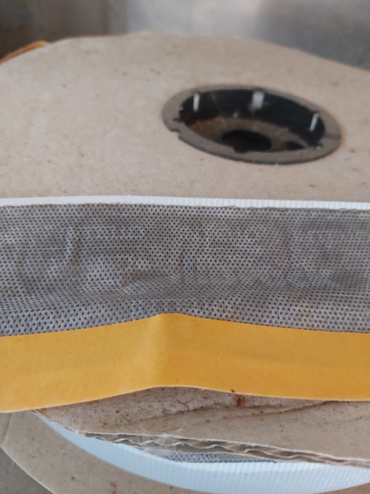 Rulle med dubbelhäftande mesh-tejp med gul klisterremsa på sidan.