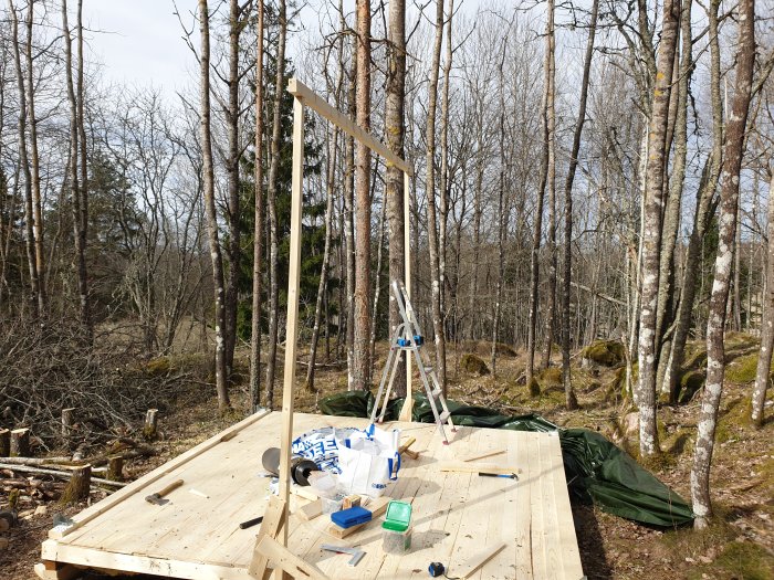 Nybyggd hustomme i trä på en plattform i en skogsmiljö, material och verktyg synliga.