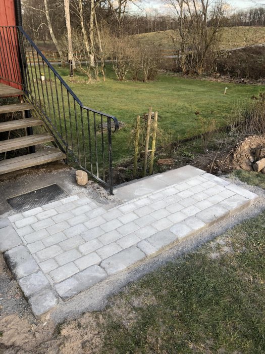 Nyrenoverad utomhustrappa med nylagda steg i sten, bredvid en gräsmatta och metallräcke.