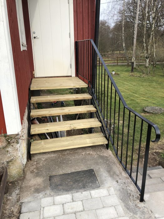 Nyinstallerade trästeg på en utomhustrappa med svart räcke vid en röd husvägg.