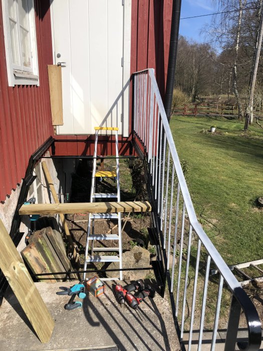 Renoverad trappa med nya trästeg bredvid hus med verktyg och målarutrustning på marken.