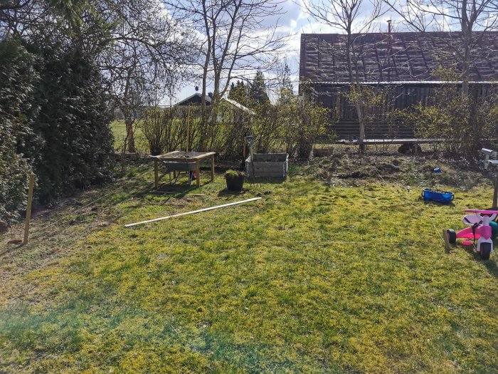 Trädgård under förändring med bortgrävd gräsmatta, trädgårdsmöbler, leksaker och utstakningslinje.