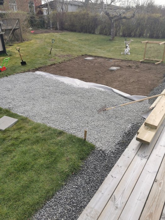 Trädgård under ombyggnad med avgrävd gräsmatta och grusytor, spadar och barnens cykel syns.