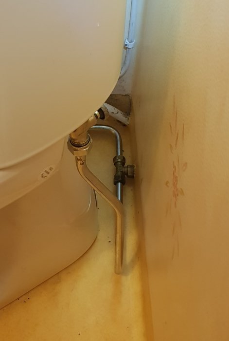 Nyinstallerad T-koppling och rör under toalett med vattenmärken på väggen.