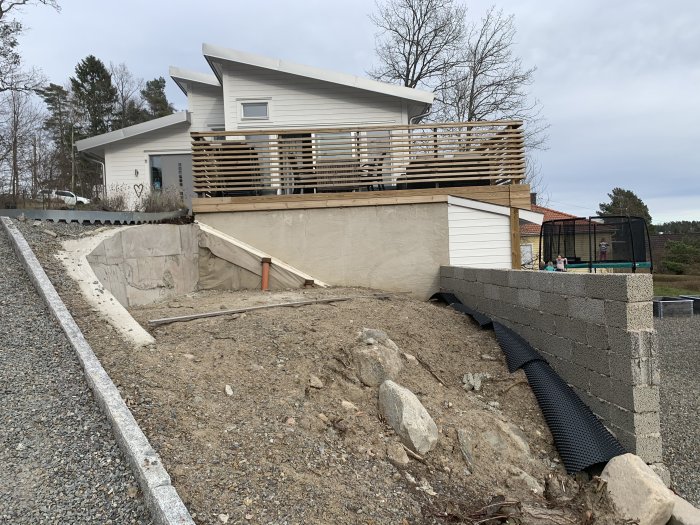 Platt yta för pool med lekablocksmur i trädgård, hus och staket i bakgrunden.