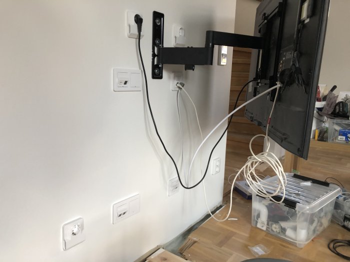 Vägg med TV-fäste och kablar, nylagade hål och eluttag.